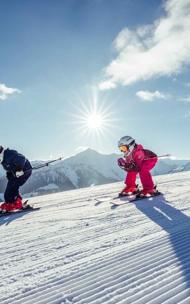 Familienurlaub im Winter in Alpbach | © Alpbachtal Tourismus | shootandstyle Eine Familie fährt gemeinsam in Hocke die Skipiste runter, im Hintergrund zu sehen die winterliche Berglandschaft | © Alpbachtal Tourismus | shootandstyle