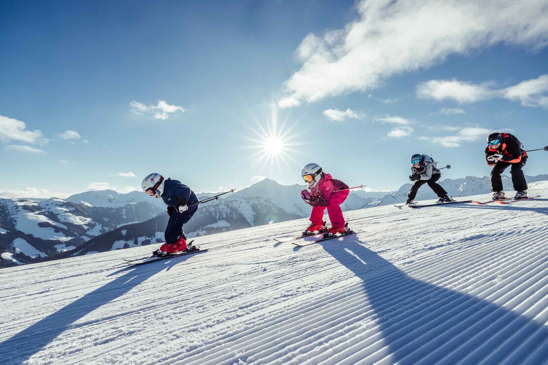 Familienurlaub im Winter in Alpbach | © Alpbachtal Tourismus | shootandstyle  Eine Familie fährt gemeinsam in Hocke die Skipiste runter, im Hintergrund zu sehen die winterliche Berglandschaft | © Alpbachtal Tourismus | shootandstyle
