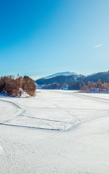 Der Reintalersee in Kramsach, eingebettet in Schnee, auf dem See Spuren für Fußgänger und Eisläufer  | © Alpbachtal Tourismus | Matthias Sedlak 
