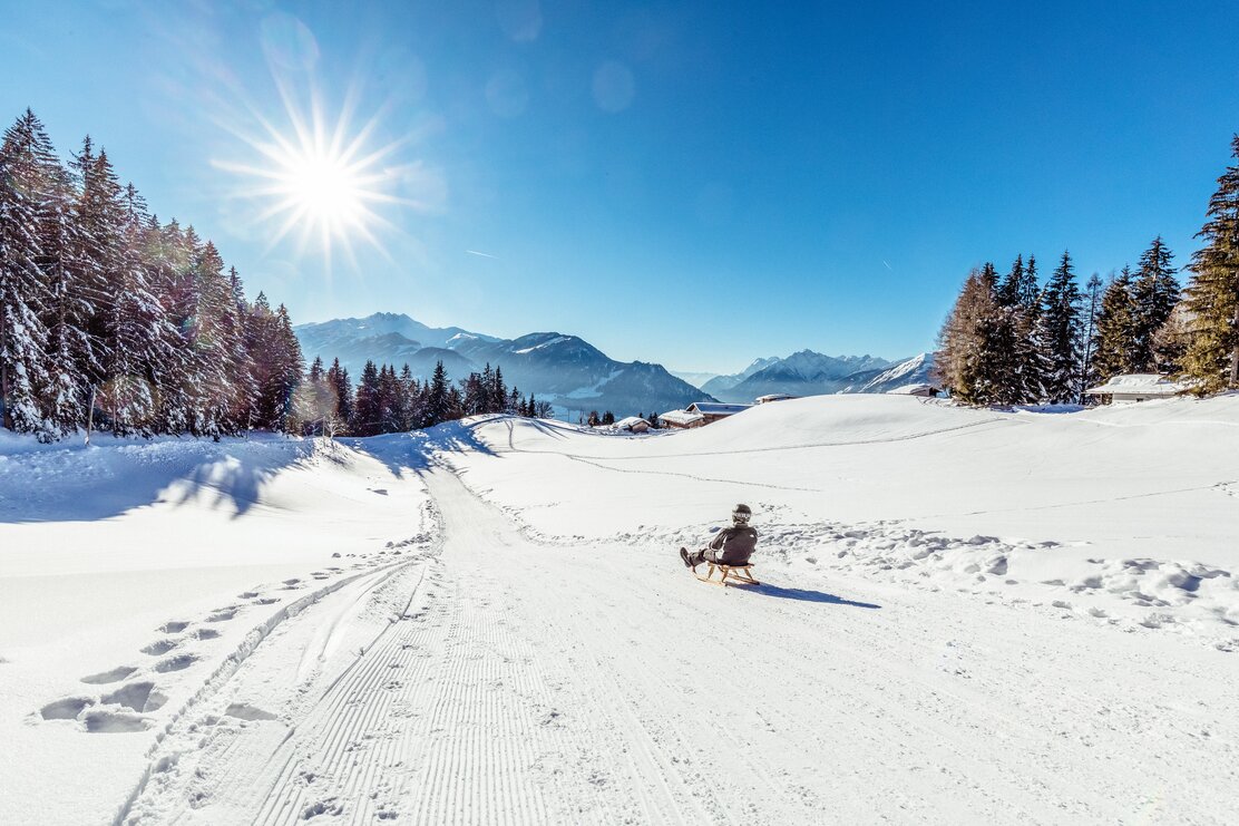 Rodeln am Reither Kogel  Ein Mann rodelt an der Rodelbahn am Reither Kogel entlang, um ihn eine verschneite Winterlandschaft, über ihm die strahlende Sonne