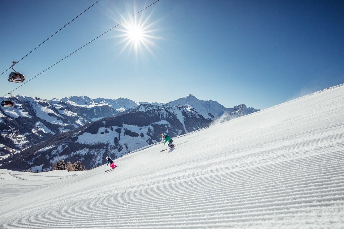 Winterurlaub im Alpbachtal  Auf diesem Bild zu sehen sind zwei Skifahrer, welche die Piste runter fahren, strahlender Sonnenschein und verschneite Winterlandschaft