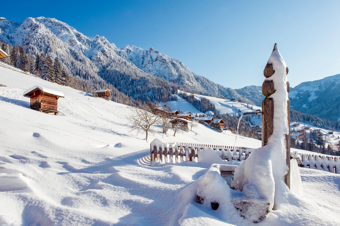 Im Vordergrund ein völlig verschneiter Brunnen, im Hintergrund die einzigartigen Häuser im Alpbacher Baustil 
