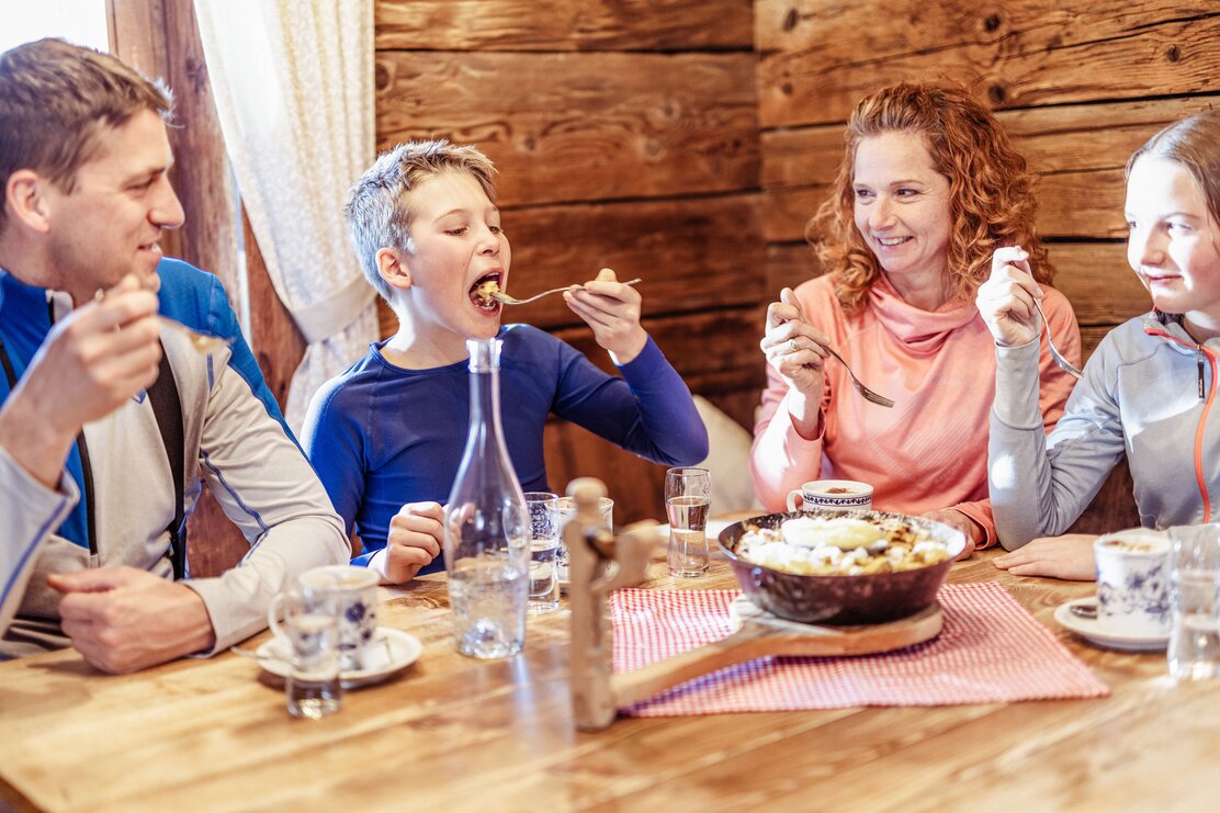 Eine Familie sitzt gemeinsam am Tisch in der Skihütte und teilt sich eine Pfanne voller Kaiserschmarrn  | © Ski Juwel Alpbachtal Wildschönau | shootandstyle 