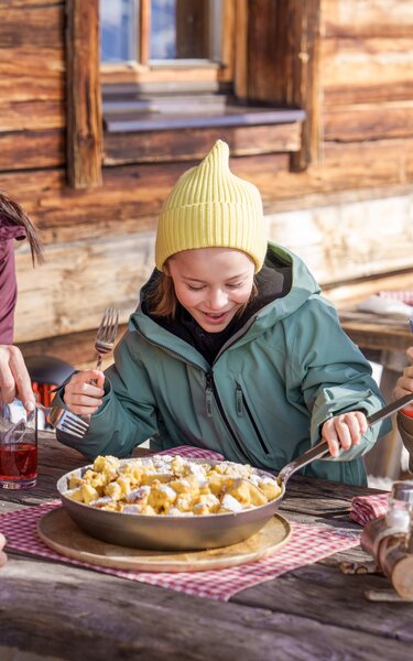 Zwei Erwachsene und zwei Mädchen auf einer Hütte beim Kaiserschmarrn essen. | © Ski Juwel Alpbachtal Wildschönau | Christoph Oberschneider