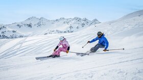 Ein Mann und eine Frau auf der Piste beim Skifahren mit Panorama im Hintergrund. | © Ski Juwel Alpbachtal Wildschönau | Christoph Oberschneider