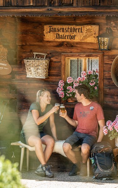 Ein paar gießt gerade ihr Bier im Garten der Jausenstation Thalerhof, im Garten blühen viele Blumen und Sträucher  | © Alpbachtal Tourismus | shootandstyle 