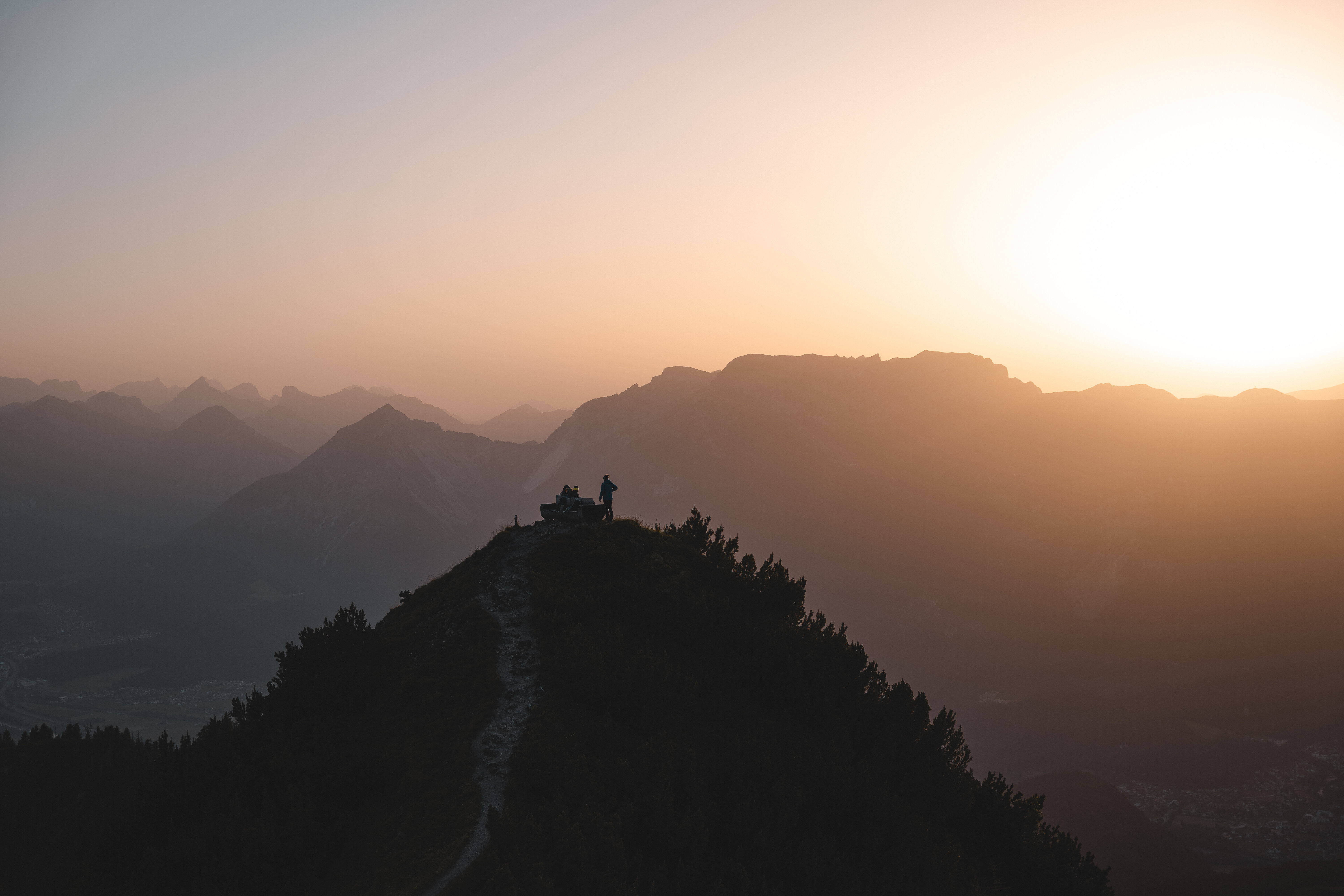 Zwei Menschen sitzen auf der Rastbank Gratlspitze und genießen den Sonnenuntergang, welcher in schönen Farben zu sehen ist  | © Alpbachtal Tourismus | Mathäus Gartner