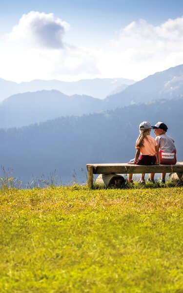Zwei Kinder (ein Mädchen und ein Junge) sitzen gemeinsam auf der Rastbank und genießen  die Aussicht auf das Alpbachtal  | © Alpbachtal Tourismus | shootandstyle