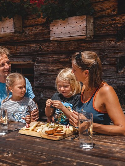 Eine Familie isst genüsslich eine Brettljause auf der Farmkehralm in Inneralpbach | © Alpbachtal Tourismus | Mathäus Gartner 