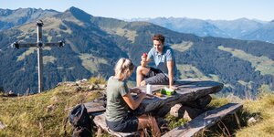 Gipfeljause Wanderung Hochstrickl Alpbach | © Alpbachtal Tourismus | shootandstyle Ein Paar genießt die Jause am Gipfelkreuz Hochstrickl in Alpbach, im Hintergrund die schöne Aussicht auf die Berge | © Alpbachtal Tourismus | shootandstyle