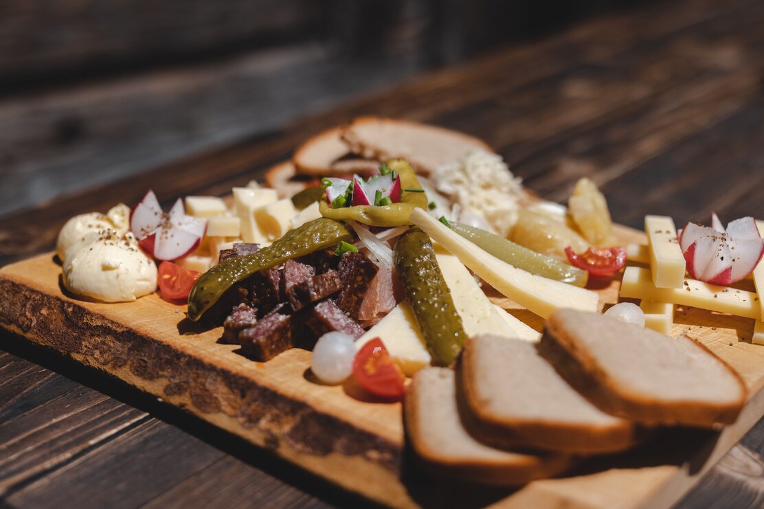 Alpbachtaler Hüttenjause auf der Farmkehralm in Inneralpbach, auf dem Holzbrett, Kaminwurzen, Käse, Essiggurken, Tomaten, Radieschen, Speck und viel mehr  | © Alpbachtal Tourismus | Mathäus Gartner 