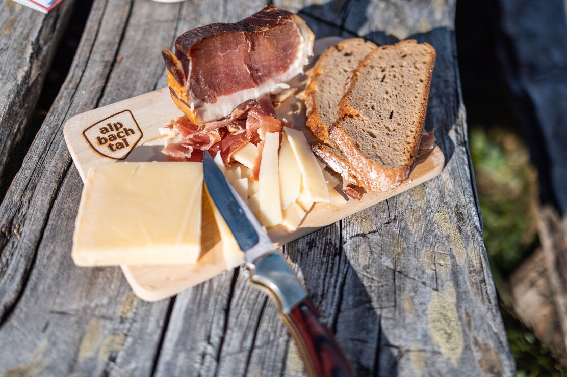 Ein Holzbrett mit dem Logo Alpbachtal eingebrannt, darauf liegt ein Stück Speck, ein Stück Käse und zwei Scheiben Brot  | © Alpbachtal Tourismus | shootandstyle 