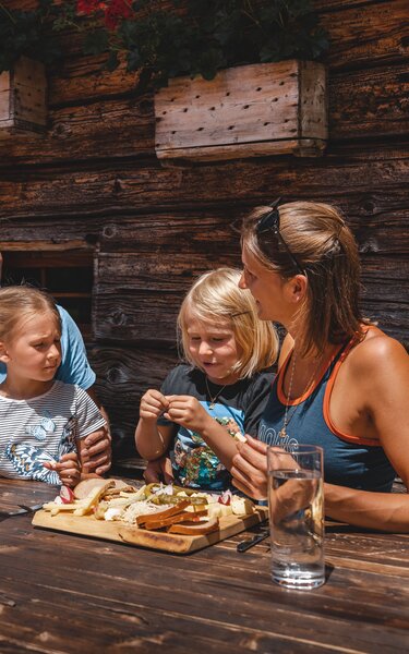 Hüttenjause auf der Farmkehralm in Inneralpbach | © Alpbachtal Tourismus | Mathäus Gartner Eine Familie isst genüsslich eine Brettljause auf der Farmkehralm in Inneralpbach | © Alpbachtal Tourismus | Mathäus Gartner