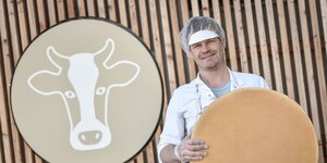 Alpbachtaler Heumilchkäserei Reith i.A. | © Alpbachtal Tourismus Ein Mann steht mit einem großem Leib Käse vor dem Logo der Alpbachtaler Heumilchkäserei in Reith i.A. | © Alpbachtal Tourismus