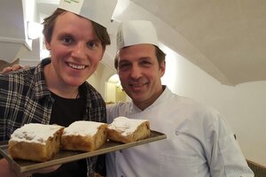 Chef Konditor Reinhard Hacker freut sich mit einem weiteren Mann über den fertig gebackenen Apfelstrudel, beide lächeln in die Kamera und halten den Teller vor die Kamera  | © Alpbachtal Tourismus 