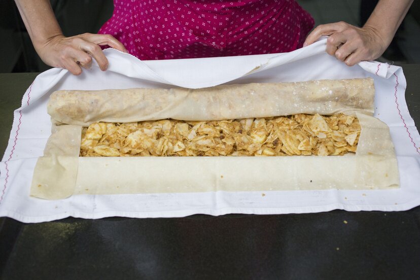 Apfelstrudel | © Tirol Werbung Eine Frau rollt den befüllten Apfelstrudel zu einer Strudelform ein | © Tirol Werbung