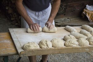 Ein Mann formt auf einem Holzbrett den Teig zu kleinen Brotstücken zurecht | © Tirol Werbung 