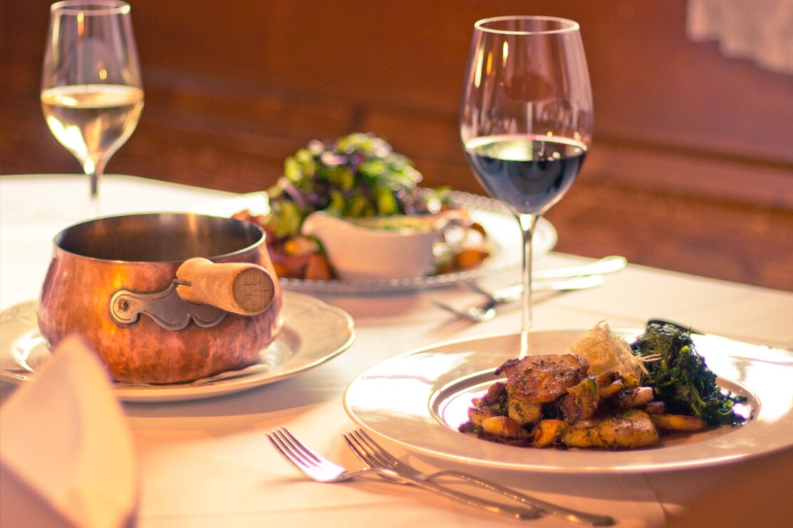 Auf dem Bild sind zwei Weingläser zu sehen, sowie drei Gerichte des Hauses  | © Hotel zur Post Alpbach 