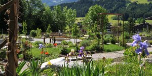 Hildegard von Bingen Garten Reith i.A. | © Alpbachtal Tourismus Im Vordergrund eine paar Lilafarbene Blumen, im Hintergrund eine kleine Holzbank, welche vom restlichen, blühenden Garten umgeben ist | © Alpbachtal Tourismus