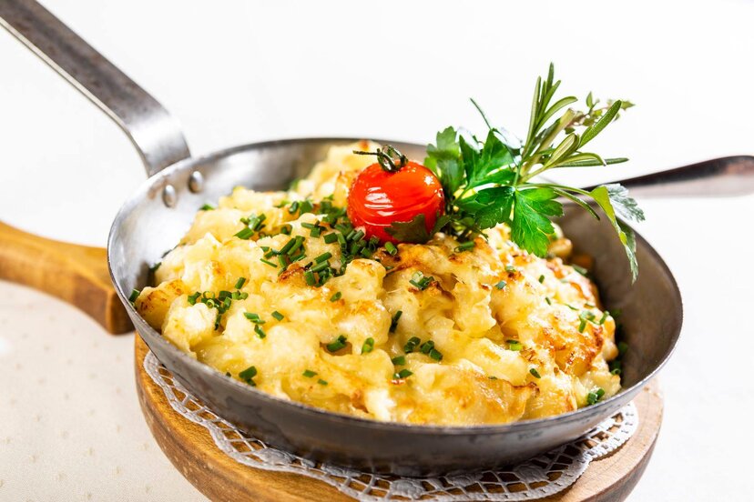 Tiroler Küche beim Stockerwirt | © Stockerwirt Reith i.A. Eine Pfanne voller Käsespätzle, garniert mit Schnittlauch, einer gedämpften Tomate, Petersilie und ein bisschen Rosmarin | © Stockerwirt Reith i.A.