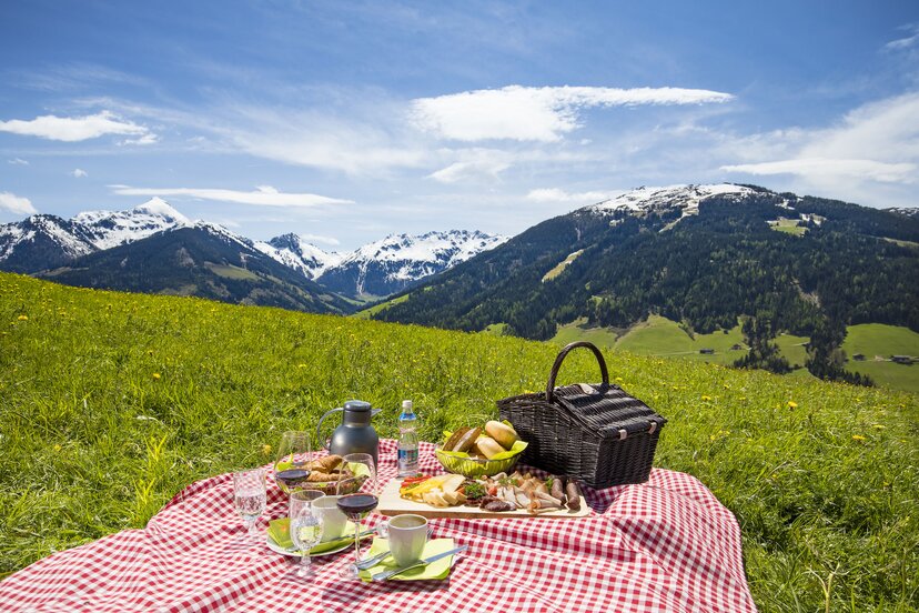 Picknick im Alpbachtal | © shootandstyle Auf einem Feld eine Picknickdecke, darauf ein Picknickkorb, Weingläser, Kaffeetassen, Teller usw., im Hintergrund die schöne Bergkulisse | © shootandstyle
