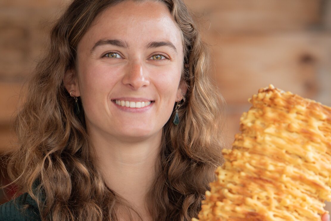 Linda Mader, die Chefin vom Familienbetrieb, Prügeltorten Mader, steht vor der Eingangstür und hält eine Original Tiroler Prügeltorte in der Hand  | © Alpbachtal Tourismus 
