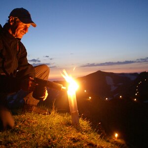 Ein Herr der gerade das Sonnwendfeuer anzündet. Es ist schon dunkel im Hintergrund. | © Alpbachtal Tourismus | Grießenböck