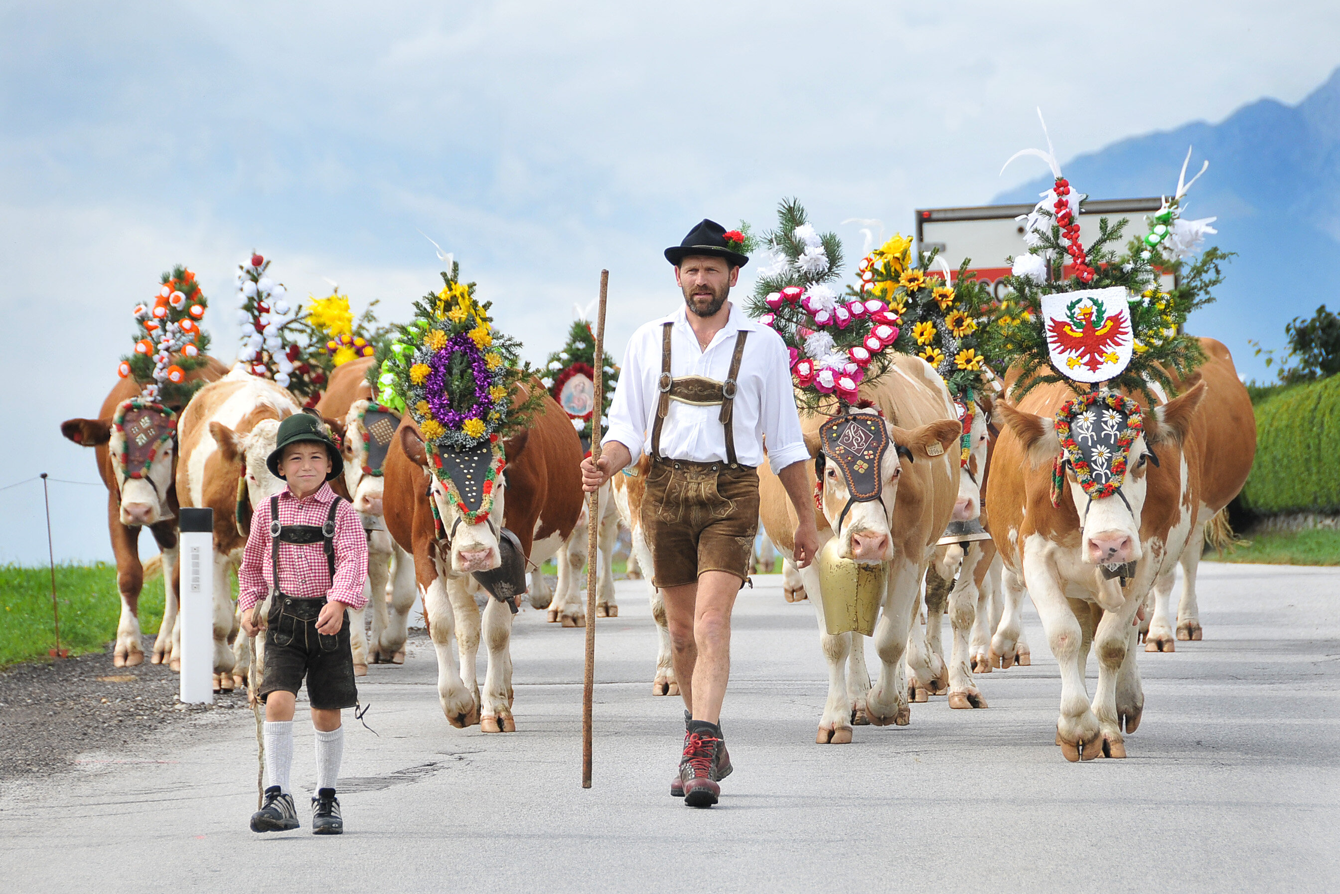 Ein Mann geht gemeinsam mit seinem Sohn beim Almabtrieb voran, dahinter viele bunt geschmückte Kühe | © Alpbachtal Tourismus