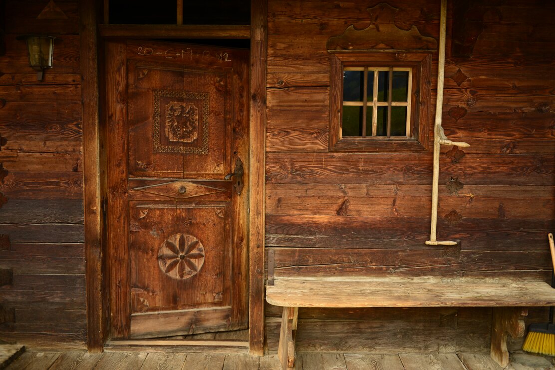 Auf dem Bild zu sehen ist eine alte gemusterte Holztür, rechts daneben befindet sich eine Holzbank  | © Alpbachtal Tourismus
