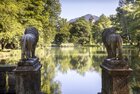 Schlosspark Matzen Löwenteich | © Alpbachtal Tourismus | Matthias Sedlak Das Bild zeigt zwei steinerne Löwenstatuen, die auf Podesten im Schlosspark Matzen stehen und auf einen ruhigen Teich blicken, der von üppigen Bäumen umgeben ist; im Hintergrund zu sehen Gut Matzen | © Alpbachtal Tourismus | Matthias Sedlak