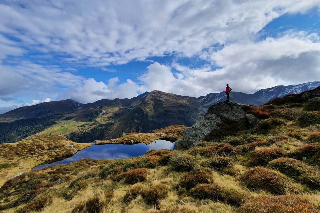 Auf diesem Bild  zu sehen ist eine Frau auf einem großen Felsen, sie genießt die Aussicht auf die Berge und den nebenliegenden  Bergteich | © Alpbachtal Tourismus 