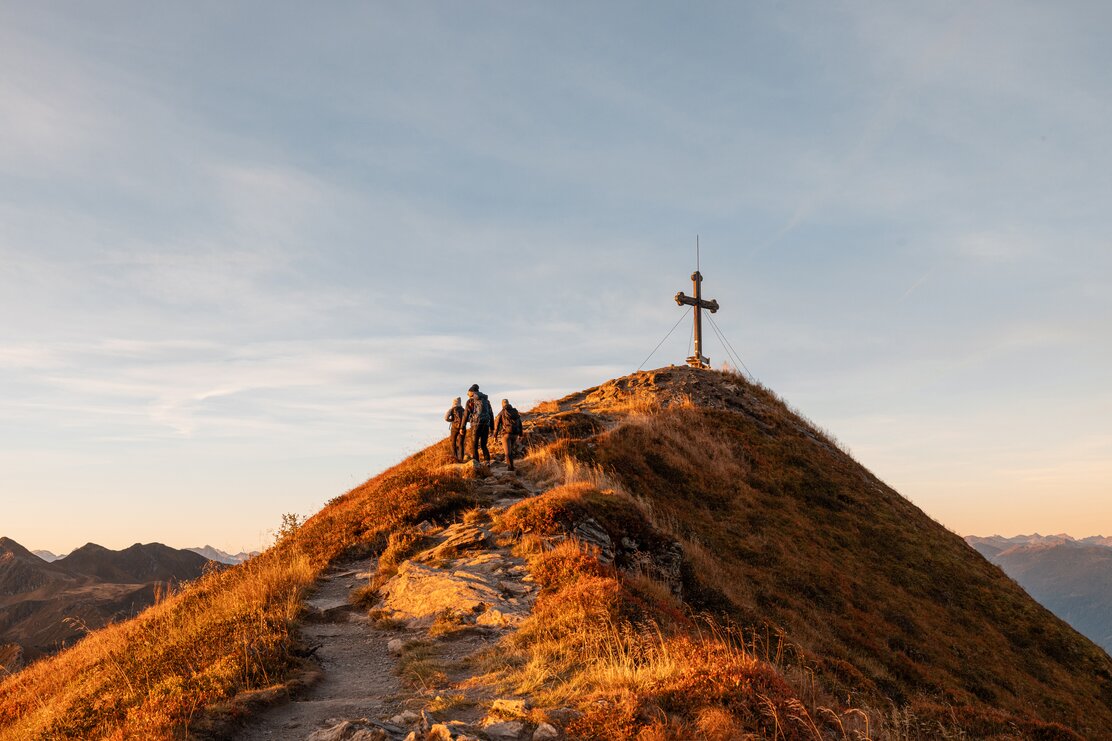 Auf diesem Bild sieht man drei Menschen, welche nur noch wenige Meter vom Gipfelkreuz Wiedersberger Horn entfernt sind  | © Alpbachtal Tourismus | shootandstyle 