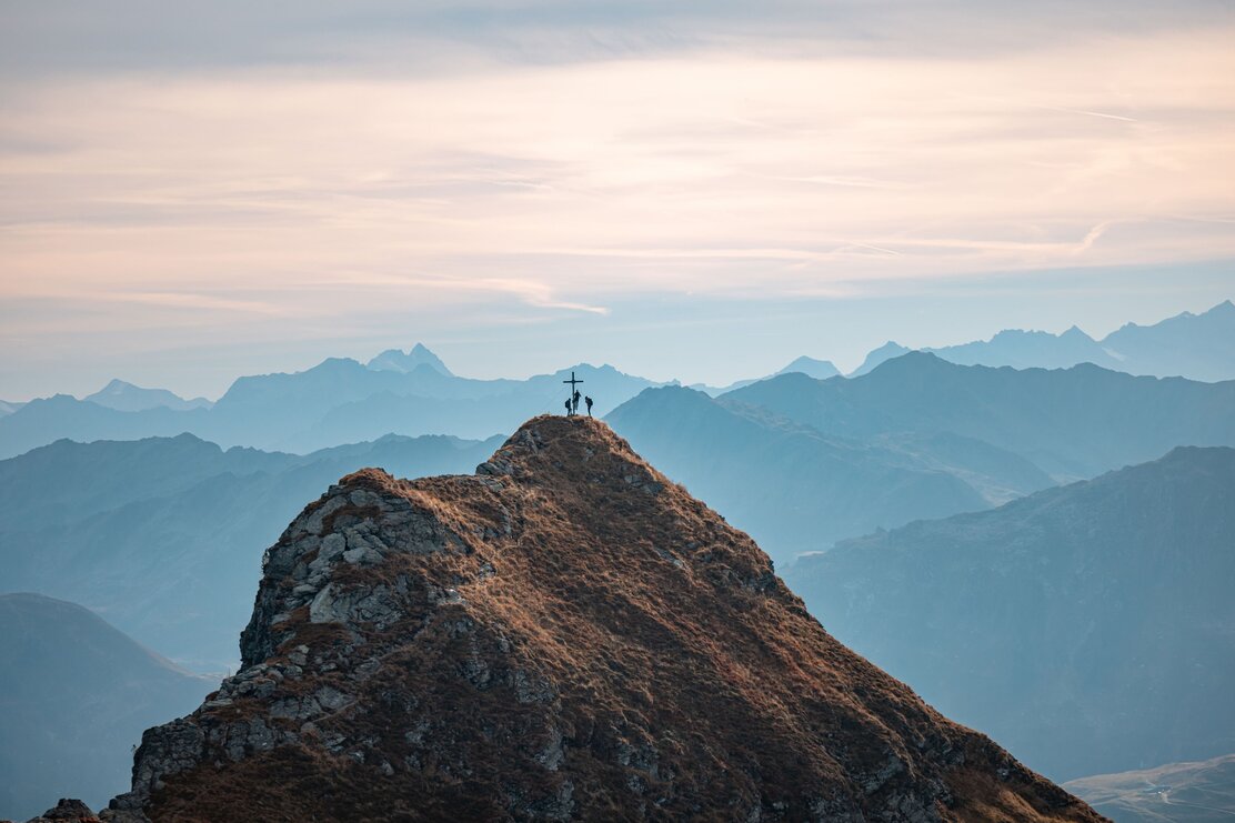 Eine Drohnenaufnahme von einer Gruppe mit drei Personen, wie sie beim Gipfelkreuz der Sagtaler Spitze ankommen, im Hintergrund die schöne Bergkulisse  | © Alpbachtal Tourismus | shootandstyle 