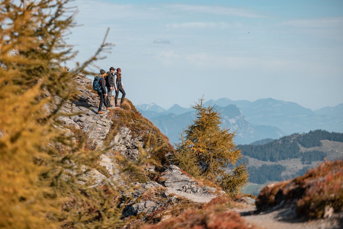 Auf diesem Bild zu sehen sind drei Personen, welche gerade auf einem großen Felsen stehen, während ihrer Wanderung, und die Aussicht genießen  | © Alpbachtal Tourismus | shootandstyle 