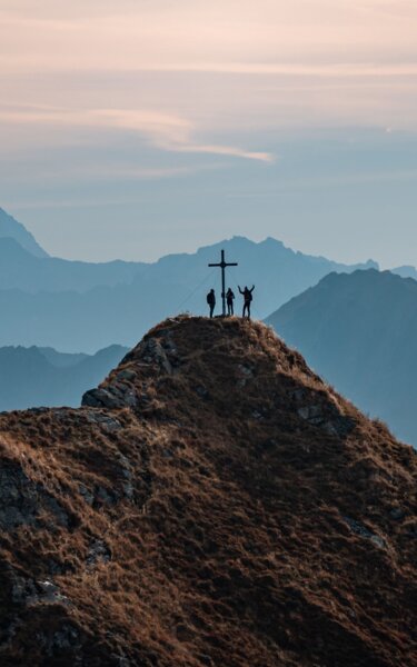 Herbstwanderung zur Sagtaler Spitze in Alpbach | © Alpbachtal Tourismus | shootandstyle Auf diesem Bild zu sehen, das Gipfelkreuz der Sagtaler Spitze in Alpbach, auf dem Gipfel befinden sich drei Personen, im Hintergrund die schöne Bergkulisse | © Alpbachtal Tourismus | shootandstyle