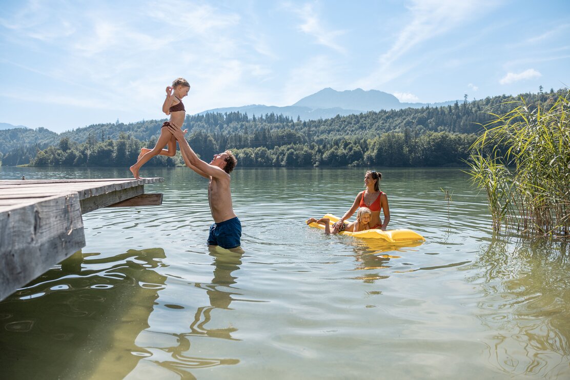 Vater hebt seinen Sohn vom Steg in den Reintalersee, die Mutter wartet bereits im Wasser mit dem Sohn auf einer Luftmatratze  | © Alpbachtal Tourismus 