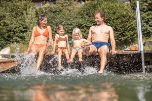 Eine Familie sitzt auf einen Steg am Reintalersee und kühlt sich die Füße im Wasser ab, alle haben Spaß | © Alpbachtal Tourismus | shootandstyle 