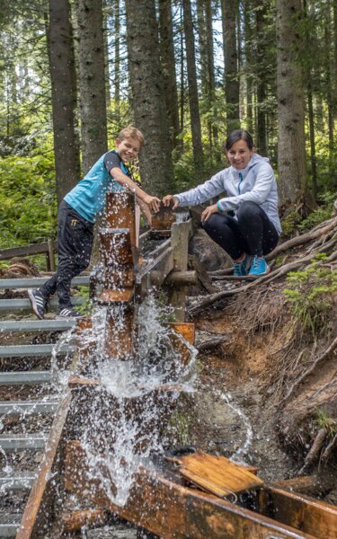 Familienspaß im Juppi Zauberwald in Reith i.A. | © Alpbacher Bergbahn | shootandstyle Eine Familie spielt gemeinsam an einem Wasserspiel im Juppi Zauberwald in Reith i.A. | © Alpbacher Bergbahn | shootandstyle
