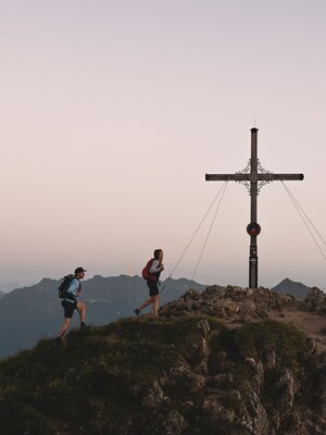 Man sieht ein Paar, das am Abend zur Gratlspitze wandert. Im Hintergrund sieht man einen schönen Sonnenuntergang, der das Gipfelkreuz beleuchtet. | © Alpbachtal Tourismus | Mathäus Gartner