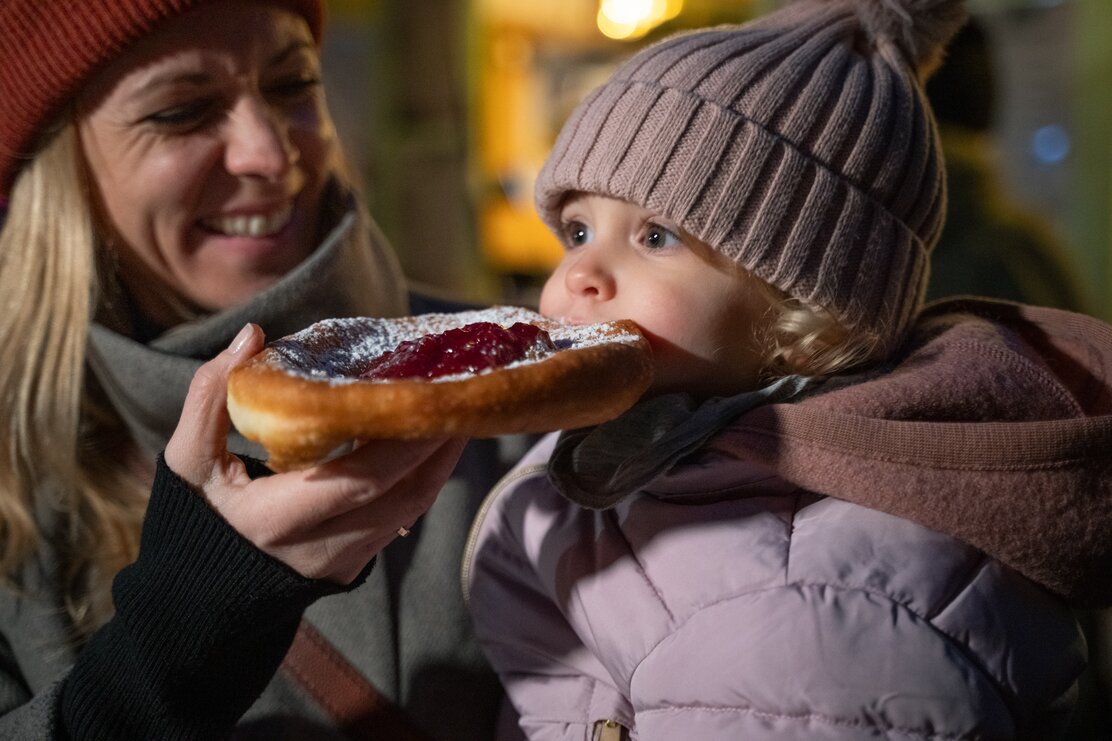 Eine Mutter lässt ihre kleine Tochter vom Tiroler Kiachl abbeißen  | © Tirol Werbung | Heinzlmeier Bert 