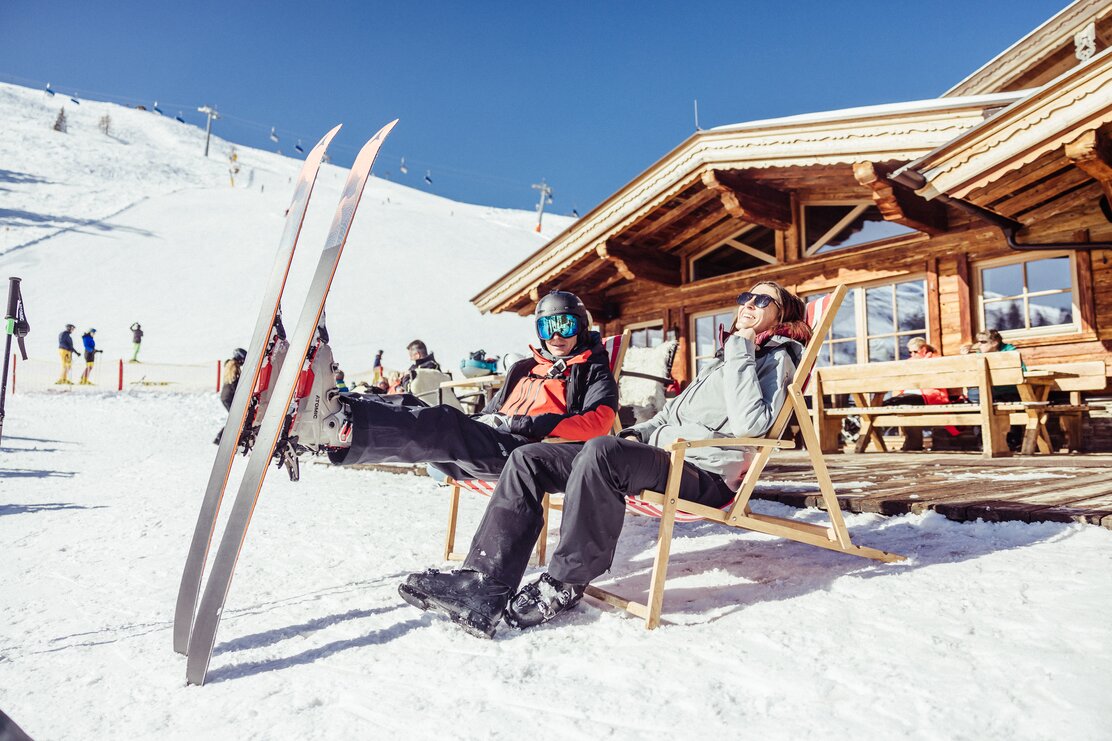 Auf diesem Bild zu sehen ist eine Frau und ein Mann,  sie genießen gerade die Sonne im Liegestuhl, im Hintergrund die Skihütte Kafner Ast in Alpbach | © Alpbachtal Tourismus | shootandstyle 