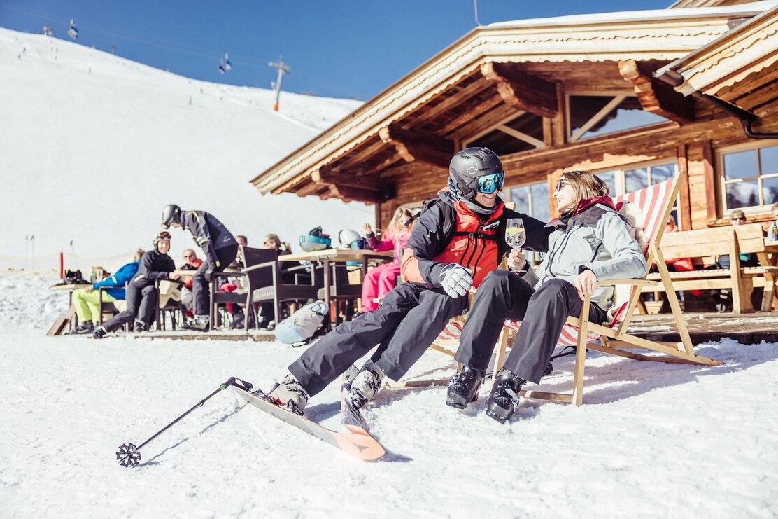Zeit zu zweit im Skigebiet Ski Juwel Alpbachtal Wildschönau  | © Alpbachtal Tourismus | shootandstyle  Auf diesem Bild zu sehen ist eine Frau und ein Mann,  sie genießen gerade die Sonne im Liegestuhl, im Hintergrund die Skihütte Kafner Ast in Alpbach | © Alpbachtal Tourismus | shootandstyle