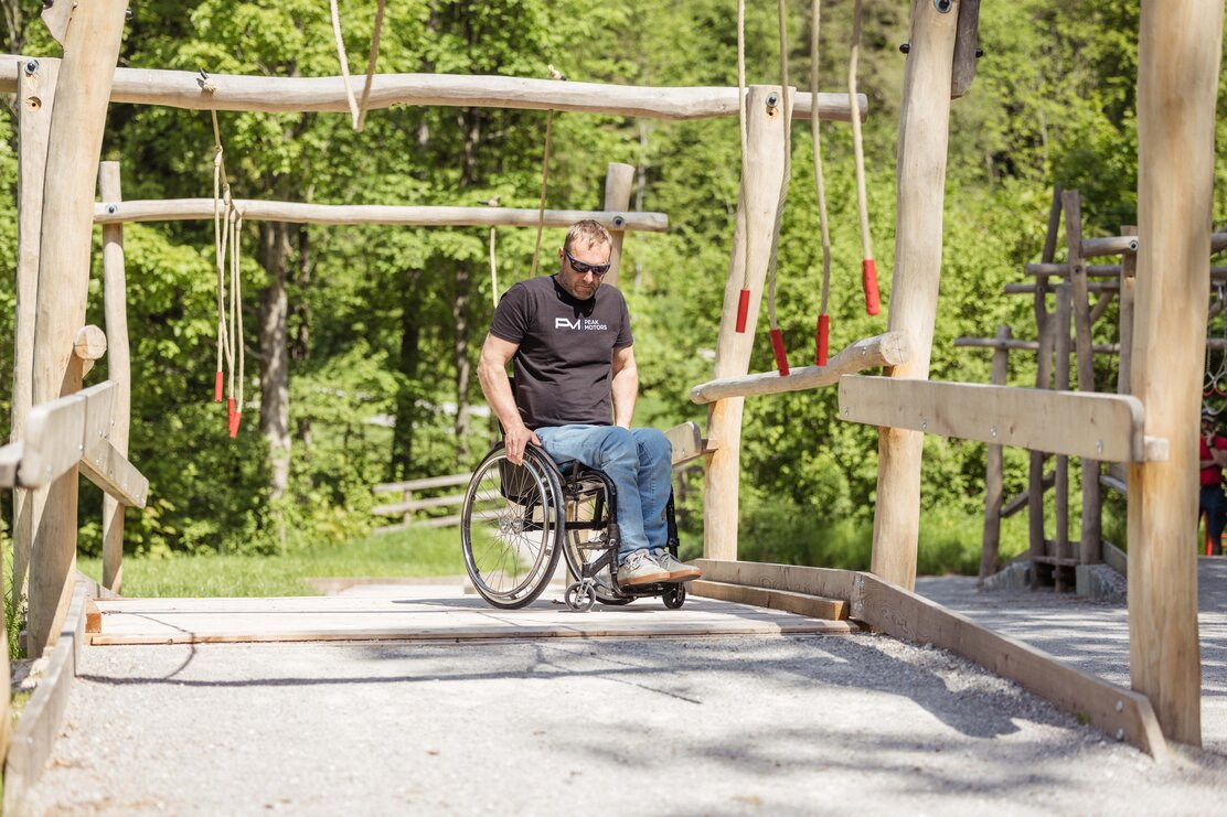 Ein Mann im Rollstuhl testet, den barrierefreien Spielplatz am Reintalersee in Kramsach, aus  | © Alpbachtal Tourismus | shootandstyle 
