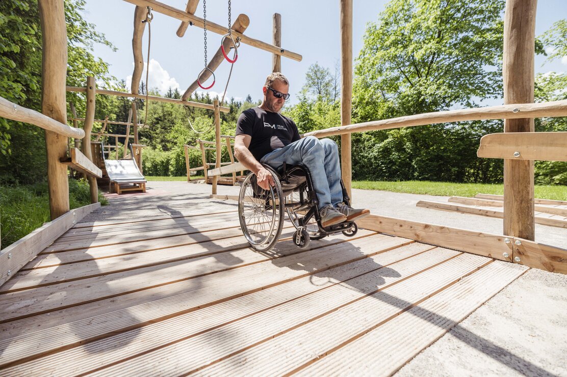 Ein Mann fährt mit seinen Rollstuhl durch den barrierefreien Spielplatz am Reintalersee in Kramsach  | © Alpbachtal Tourismus | shootandstyle 