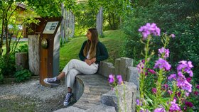 Eine Frau sitzt entspannt auf einer Rastbank im Hildegard von Bingen Garten in Reith  und hört sich die Rastbank G'schichten an | © Alpbachtal Tourismus