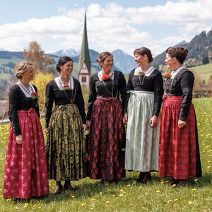Man sieht fünf Frauen, die, ein Kassettl tragend, auf einem Feld vor der Kirche stehen. | © Alpbachtal Tourismus | Maximalgrafik