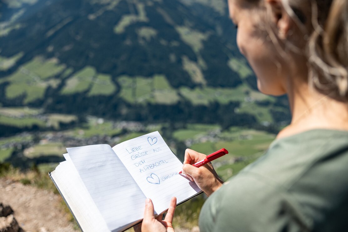 Auf diesem Bild zu sehen ist eine Frau, welche gerade etwas in das Gipfelbuch, auf der Gratlspitze, einträgt | © Alpbachtal Tourismus | shootandstyle 