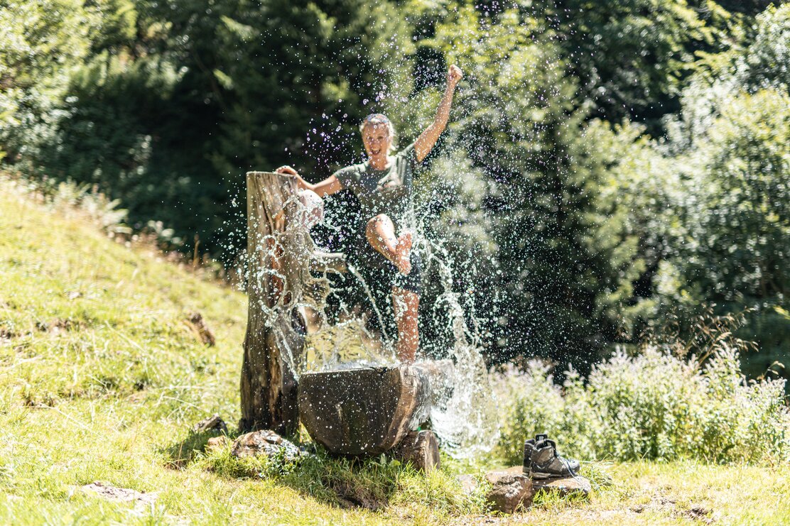 Auf diesem Bild zu sehen ist eine Frau am Brunnen beim Hösljoch in Alpbach, welche sich im Brunnen erfrischt  | © Alpbachtal Tourismus | shootandstyle 