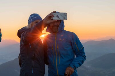 Auf diesem Bild sieht man eine Frau und einen Mann, welche ein Selfie machen, im Hintergrund der schöne Sonnenaufgang  | © Alpbachtal Tourismus | shootandstyle 